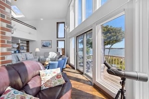 A spacious living area with a leather sofa, a dining table, and a large window overlooking a body of water.