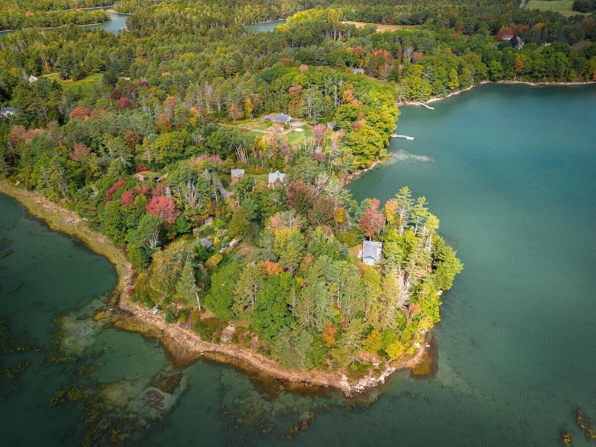Luchtbeeld van een afgelegen eiland met dicht bos, een kleine steiger en enkele gebouwen.