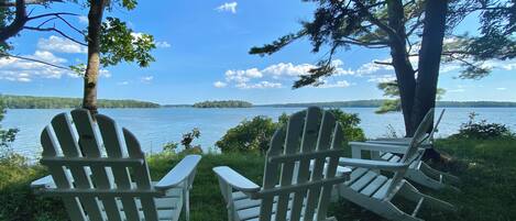 Two Adirondack chairs facing a lake with a forested shoreline.