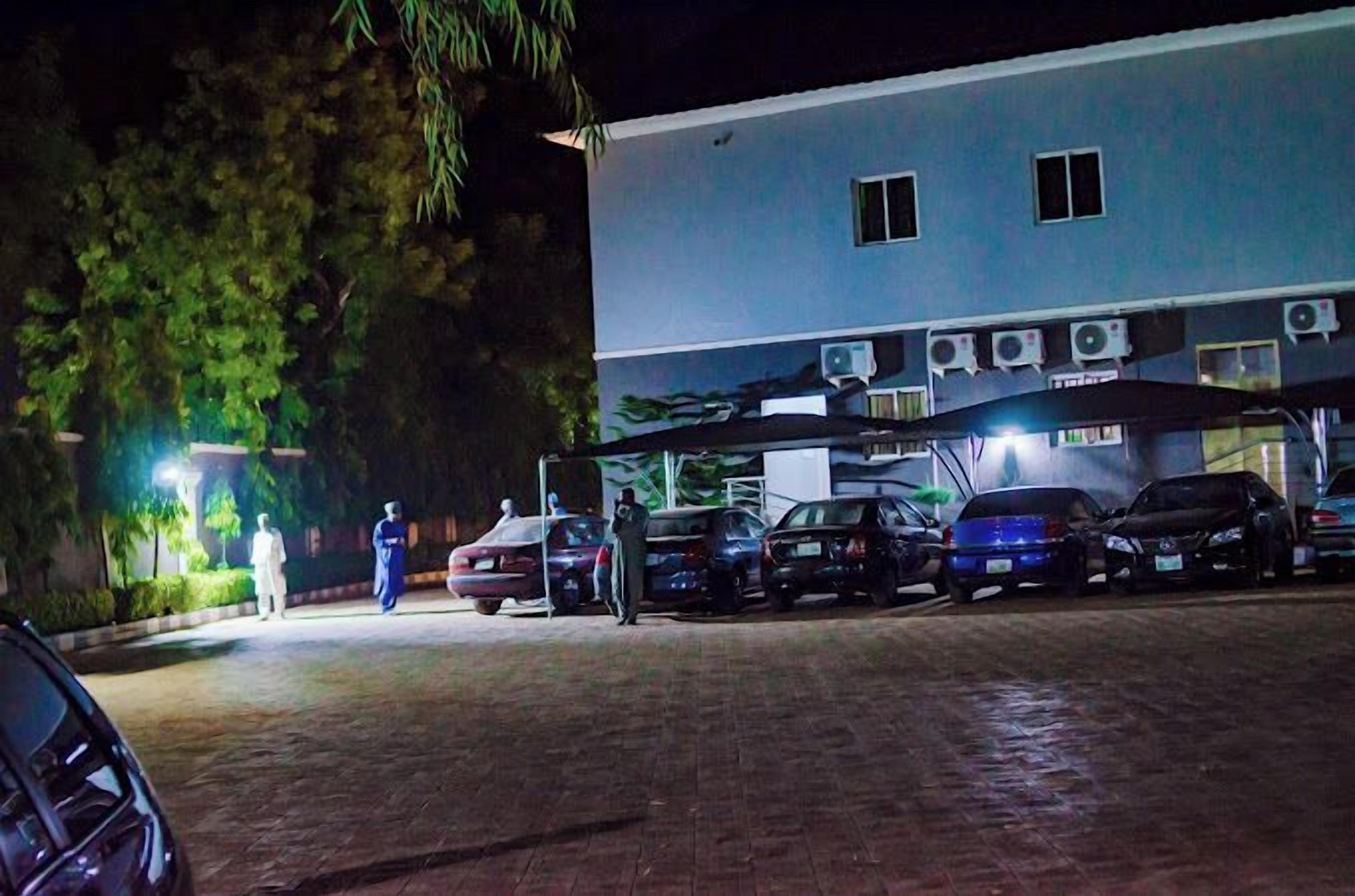 A building with multiple air conditioning units, parked cars, and a covered parking area at night.