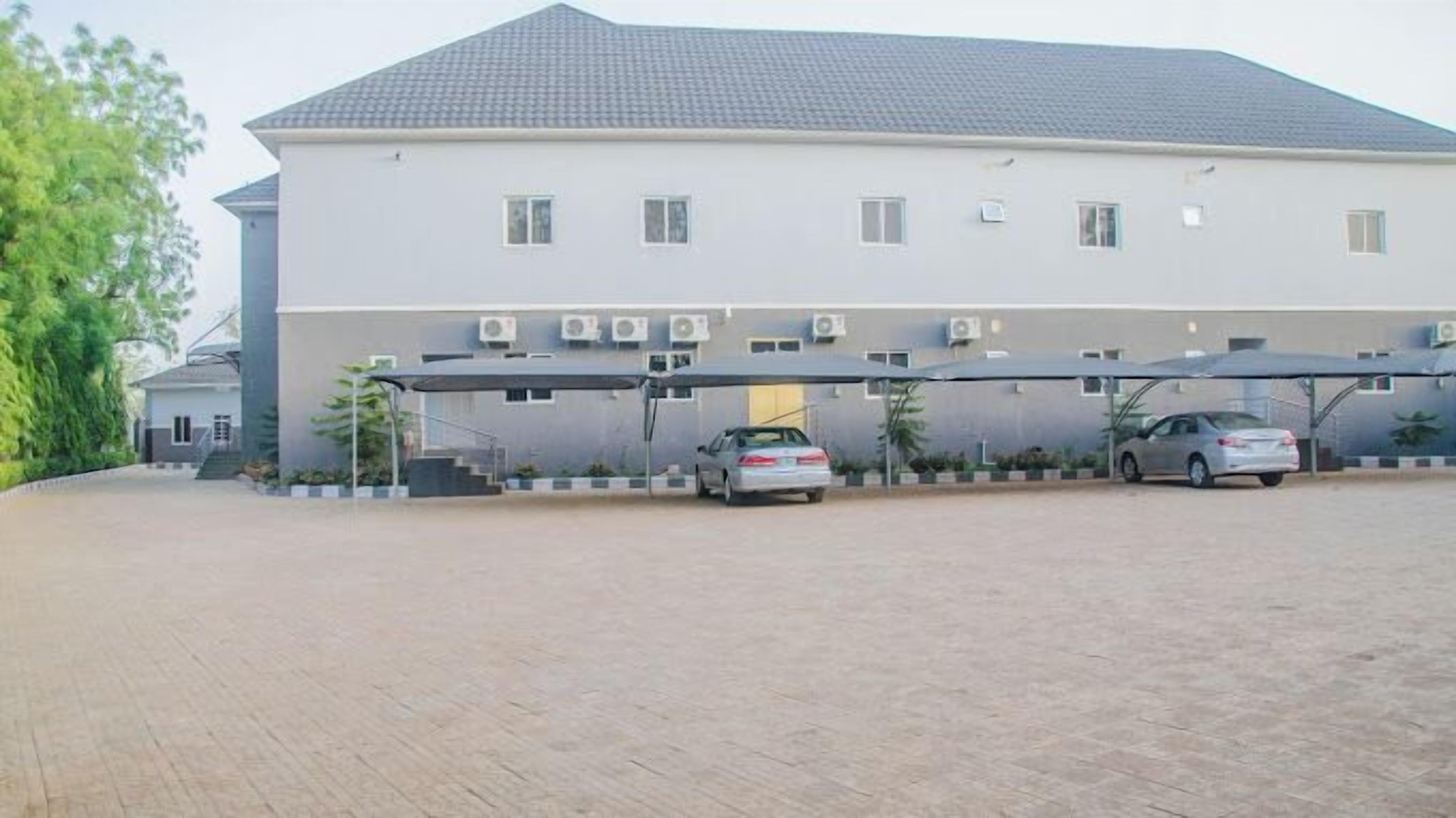 A building with a flat roof, multiple air conditioning units, and a covered parking area with two cars.