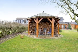 A gazebo with a roof, wooden walls, and a stack of firewood inside.