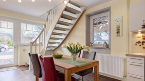 Un comedor con una mesa de madera, sillas, un florero con flores, una escalera y una ventana con vistas al exterior.