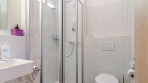 A bathroom with a glass shower enclosure, a white sink with a soap dispenser, a toilet, and a trash can. - Room 'Zimmer 2' with Shared Garden and Wi-Fi (Reichenau)