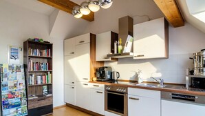 A modern kitchen with white cabinetry, a built-in oven, a coffee maker, and a bookshelf filled with books. - Room 'Zimmer 2' with Shared Garden and Wi-Fi (Reichenau)