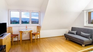 A room with a wooden floor, a grey sofa, a dining table with chairs, and a TV on a cabinet. - Room 3 with Shared Garden and Wi-Fi (Reichenau)