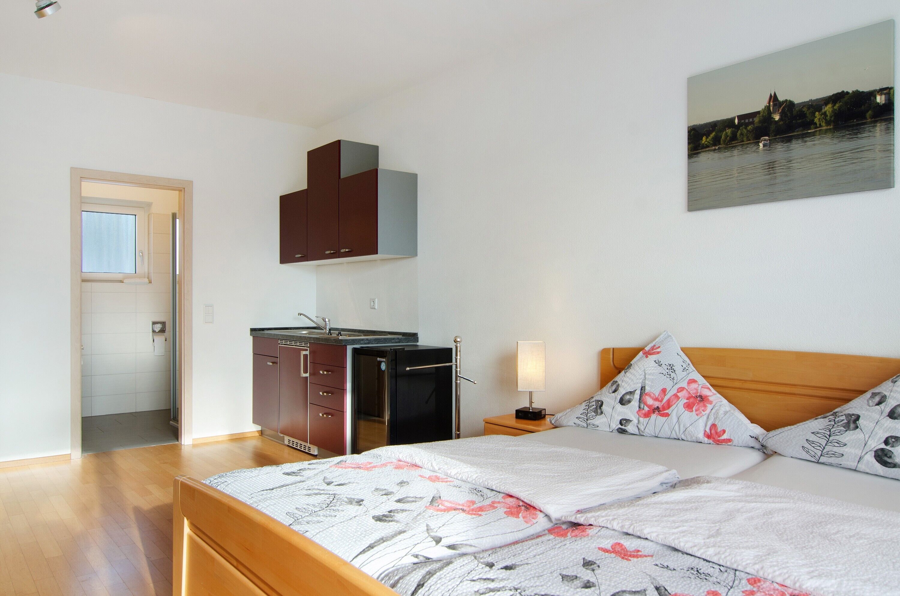 A bedroom with a bed, a nightstand, a lamp, a window, and a view of a building across the water.