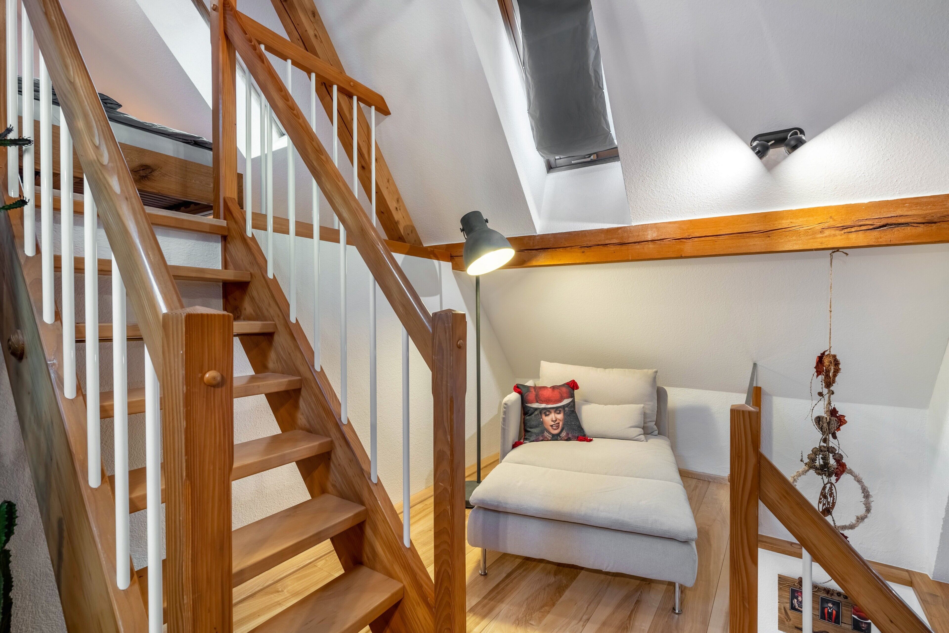 Ein Schlafzimmer im Loft-Stil mit einer Holztreppe, einem Bett mit Zierkissen und einem hängenden Ornament.