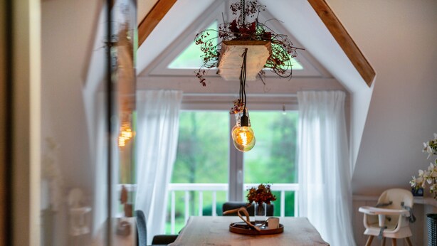 Un comedor con una mesa de madera, sillas, una lámpara colgante y vistas a la vegetación exterior.
