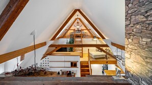 Un interior de varios niveles con vigas de madera a la vista, pared de piedra y una escalera que conduce a una zona superior.