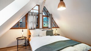 Un dormitorio con techo inclinado, una cama con almohadas y una colcha, dos lámparas de noche y un colgador con luz.