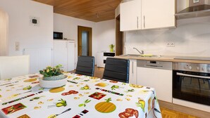 A modern kitchen with white cabinets, a built-in oven, and a dining table with a fruit-themed tablecloth.