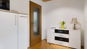 A room with a wooden ceiling, a white cabinet with drawers, a door with a glass panel, and a microwave on the wall.