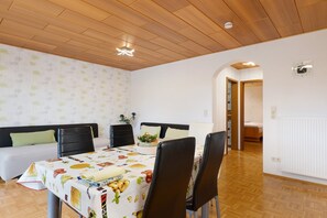 A dining area with a table set for four, a sofa, and a bed in the background.