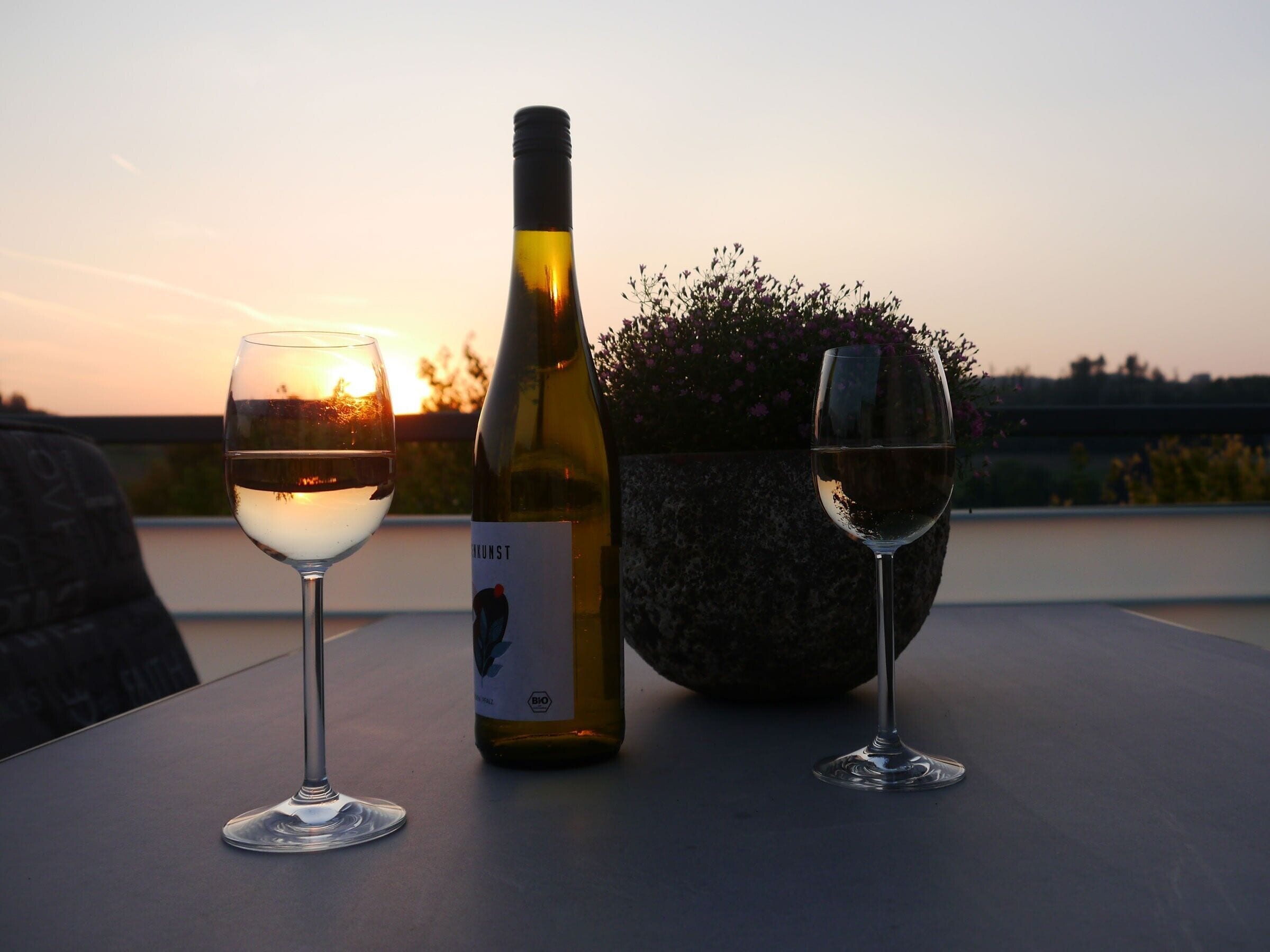 Zwei Weingläser und eine Flasche auf einem Tisch mit Blick auf einen Sonnenuntergang.