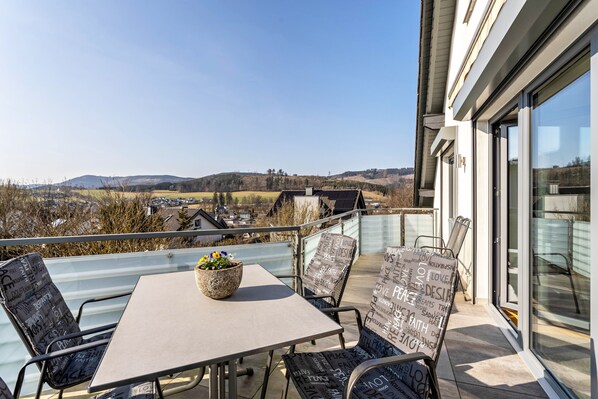 A balcony with a table and chairs, a potted plant, and a view of the countryside.