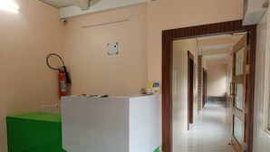 Zona de recepción con mostrador verde y blanco, un extintor y un pasillo que conduce a otras habitaciones.