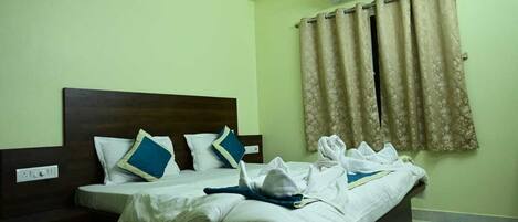 A hotel room with a bed, a nightstand, an air conditioning unit, and a window with curtains.