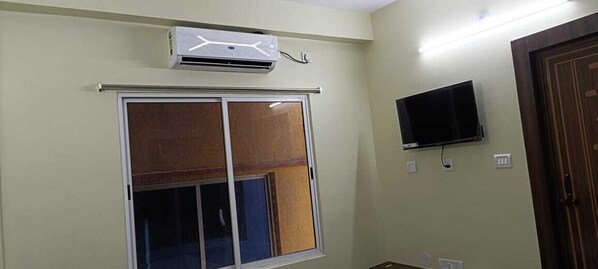 A room with a sliding door, an air conditioning unit, a mounted television, and a wooden door. - Venture Inn Puri (Puri)