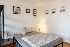 A bedroom with a bed, pillows, a bedside table with a lamp, and wall art depicting cityscapes.