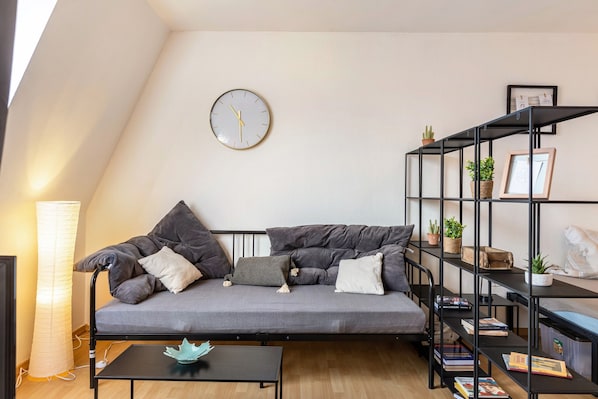 A modern living room with a sofa, a coffee table, a bookshelf, and a wall clock.