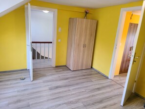 Une pièce aux murs jaunes, avec une armoire en bois, une porte blanche et un escalier menant à une autre pièce.
