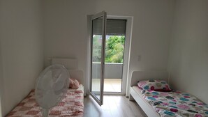 Une chambre avec deux lits, un ventilateur et une porte-fenêtre coulissante donnant sur un balcon.