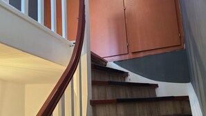 Un escalier en bois avec une rampe, un palier avec une porte, et une lucarne au-dessus.