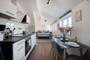 Una cocina moderna con una isla central, un comedor con una mesa y sillas, y un dormitorio con una cama y mesitas de noche.