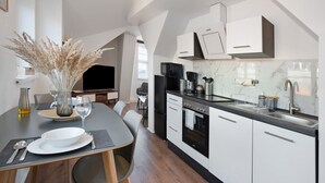 A modern kitchen with white cabinets, a black countertop, and a dining area with a table set for two. - Apartment 'Domblick Deluxe' with Wi-Fi (Meißen)