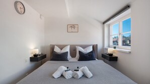 A neatly made bed with towels, a clock, a framed picture, and a window with a view. - Apartment 'Domblick Deluxe' with Wi-Fi (Meißen)