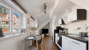 A modern kitchen with white cabinets, a dining table with chairs, a TV, and a view of buildings outside. - Apartment 'Domblick Deluxe' with Wi-Fi (Meißen)