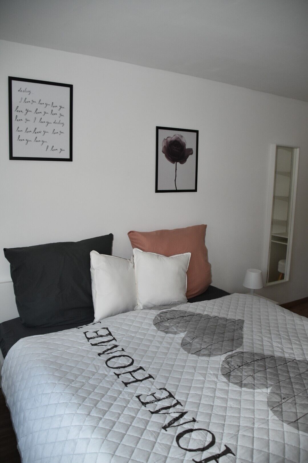 Une chambre à coucher avec un lit, des oreillers, une citation encadrée et une fleur encadrée.