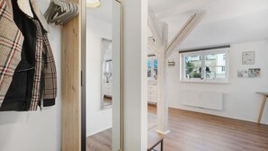 Ein Zimmer mit Holzboden, einem Spiegel, einem Kleiderständer mit Jacken, einem Fenster mit Aussicht und einer Heizung.