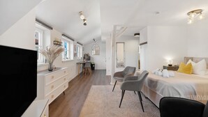 Ein modernes Hotelzimmer mit einem großen Bett, einem Schreibtisch, einem Sessel und einem Fernseher.