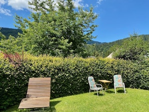Un jardín con un banco de madera, dos sillas y una pequeña mesa.