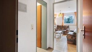Un couloir mène à un espace de vie comprenant un canapé, une table basse et une lampe.