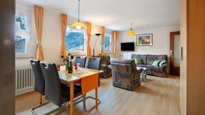 Ein modernes Wohnzimmer mit Essbereich, einer Sofagarnitur und einem an der Wand montierten Fernseher.