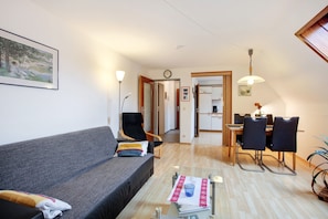 Een moderne woonkamer met een bank, een eettafel met stoelen, een salontafel en een keuken op de achtergrond.
