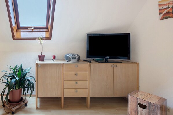 A room with a wooden cabinet, a television, a potted plant, and a small table.