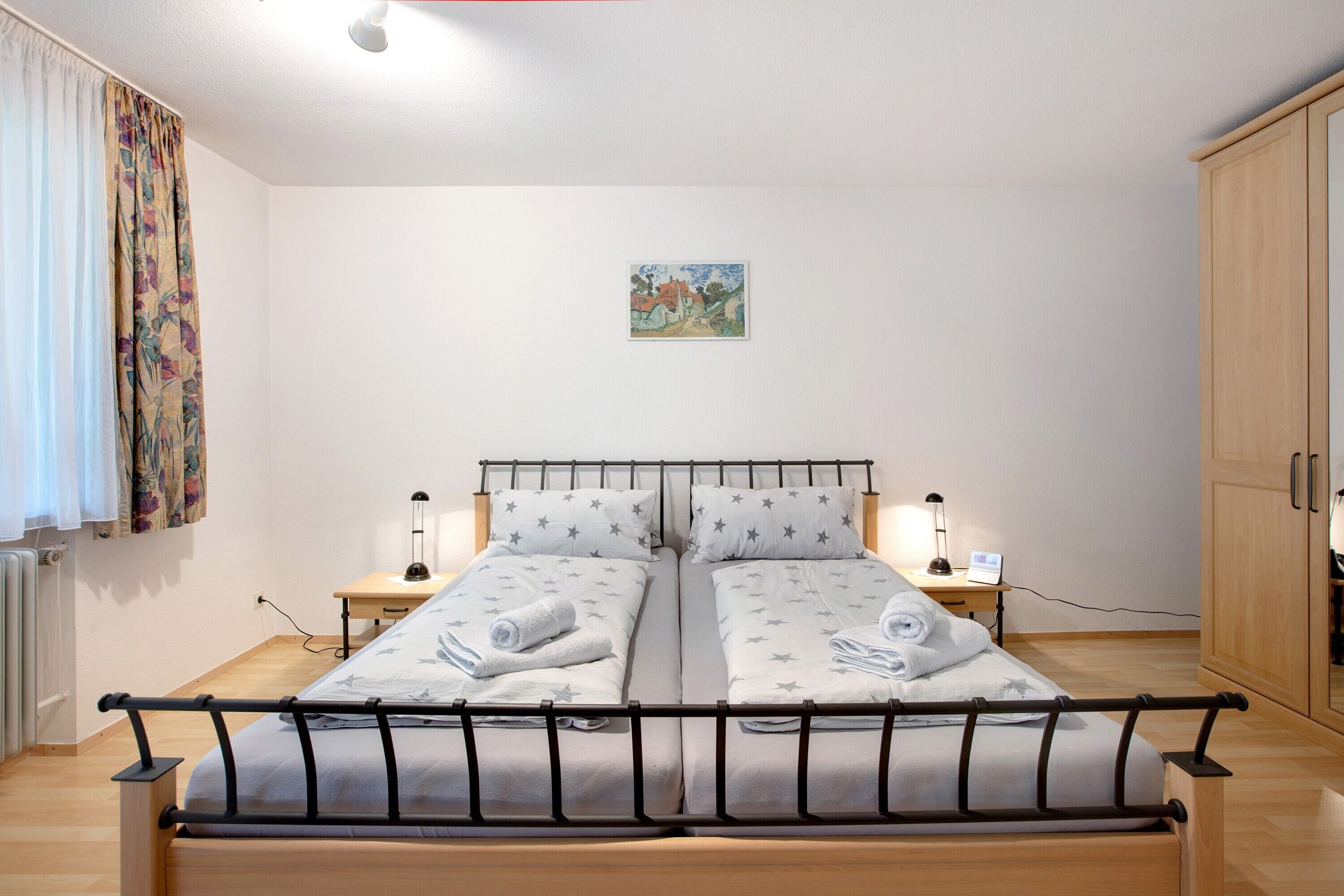 Un lit double avec une literie à motifs d’étoiles, des lampes de chevet, une petite table et une armoire en bois.