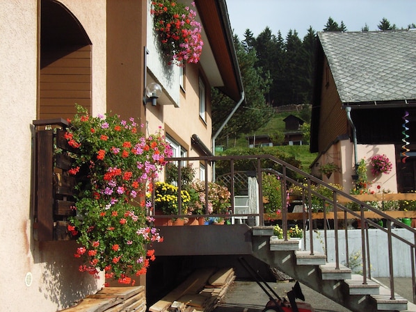 A building with a staircase leading to a landing, surrounded by flower boxes and potted plants. - Apartment 'B, 66 sqm' with Shared Garden, Balcony and Wi-Fi (Sankt Blasien)