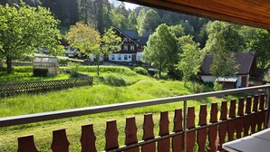 A balcony with a view of a green landscape, houses, and a wooden fence. - Apartment 'B, 66 sqm' with Shared Garden, Balcony and Wi-Fi (Sankt Blasien)