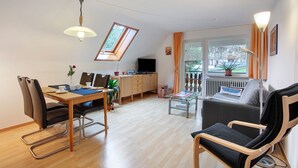 A modern living room with a dining area, a sofa, a TV, and a window with curtains. - Apartment 'B, 66 sqm' with Shared Garden, Balcony and Wi-Fi (Sankt Blasien)