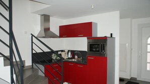Una cocina compacta con armarios rojos, una campana extractora de acero inoxidable y un microondas integrado.