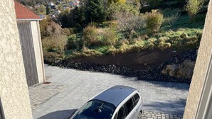 Un coche plateado estacionado en una entrada con un muro de piedra y vistas a una zona residencial.