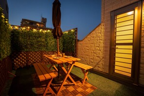 Eine Terrasse mit Holztisch und Bänken, umgeben von einer Ziegelmauer und einem Hecken.