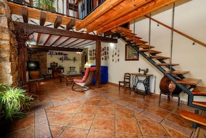 Un intérieur rustique avec un escalier en bois, un mur en pierre et un coin salon confortable agrémenté d’un fauteuil à bascule.