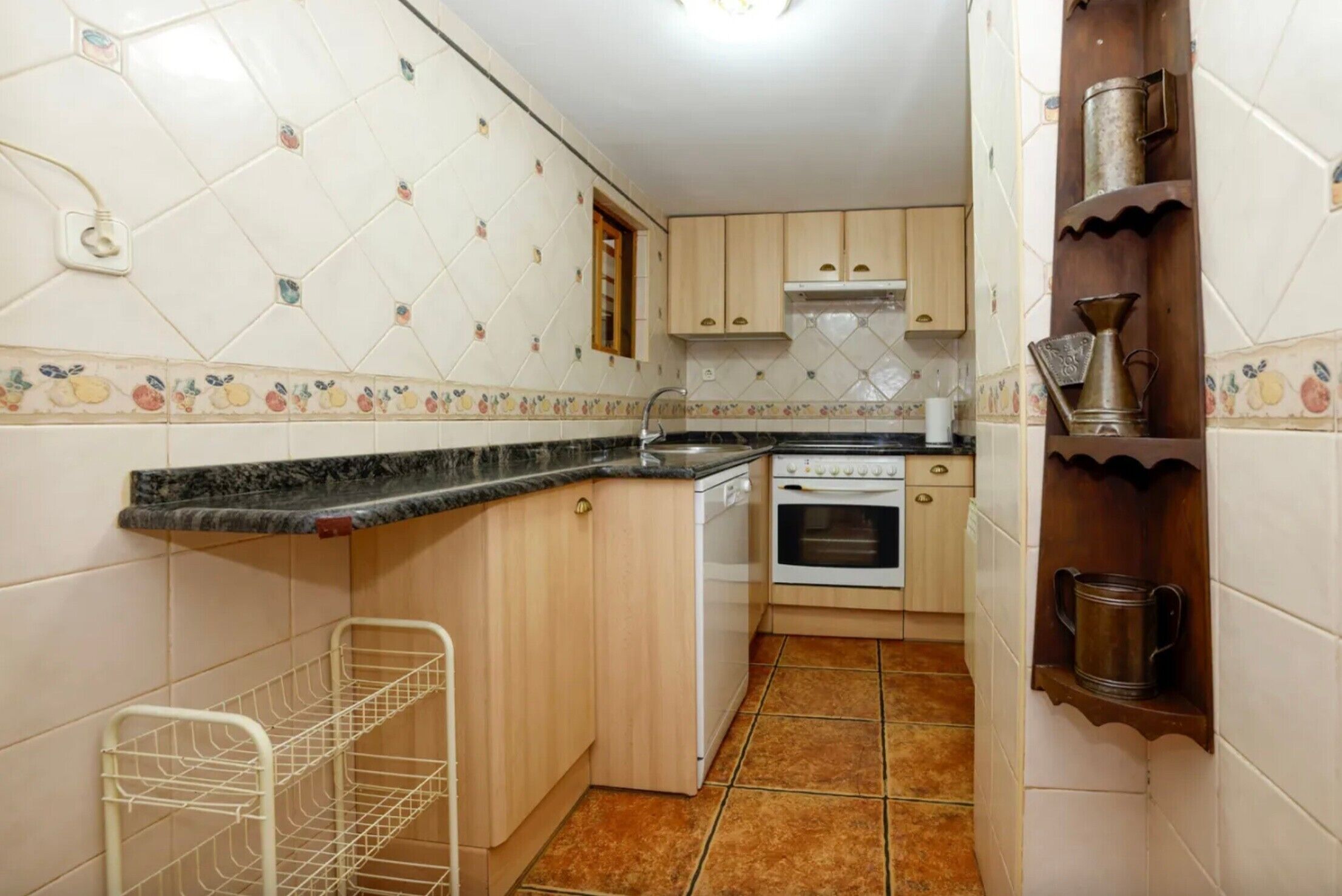Een compacte keuken met een vaatwasser, oven en een klein schap met metalen bakken.