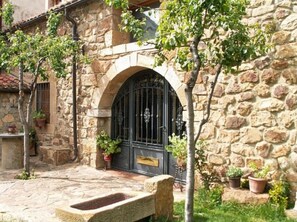 Un bâtiment en pierre doté d’une grande entrée en arc de cercle, de plantes en pot et d’un banc en pierre.